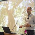 Alex Antonelli delivers the keynote lecture for BUC. He is in front of a screen showing an image of a large tree.