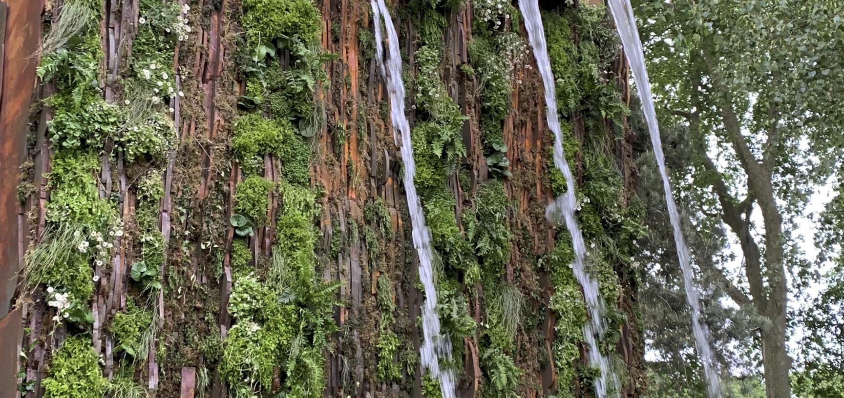 A picture of high garden walls, with large fountains cascadeing water over greenery.