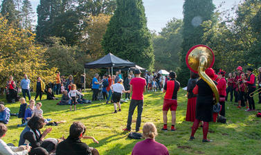 Many people gathered for the Autumn Fair at Harcourt Arboretum. They are seated on the grass watching a performance by a brass band.