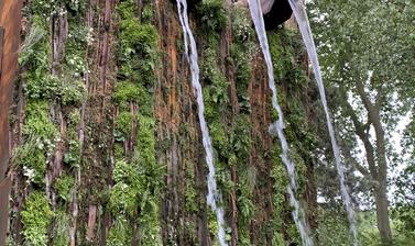 A picture of high garden walls, with large fountains cascadeing water over greenery.