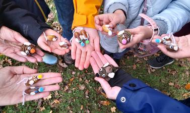 Eight outstretched adult and child hands, each holding one or two colourful mice crafted out of acorn and pinecone bodies, pompom noses, googly eyes, felt ears, and yarn tails. 